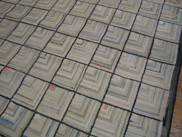 Textured gray and cream rug featuring a dark grid over geometric concentric square patterns on wood flooring.