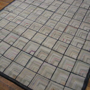 Muted neutral rug featuring a dark-lined diamond grid and internal chevron patterns on wood plank flooring.