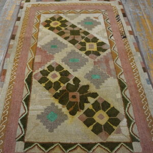 Geometric hooked rug in olive green, rose, and tan on distressed wooden plank flooring.