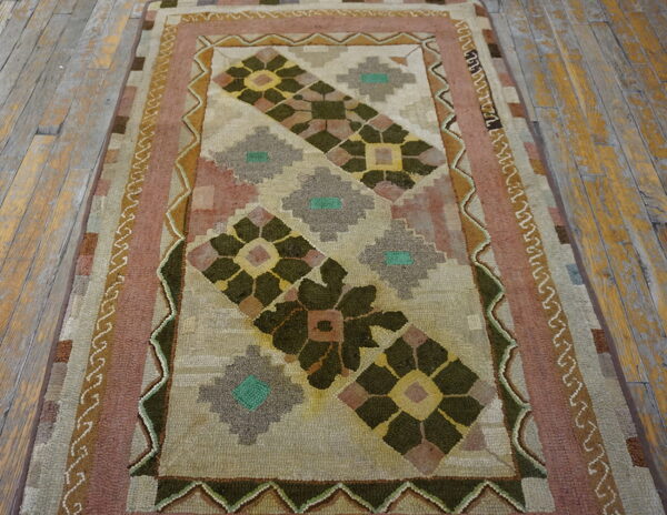 Geometric hooked rug in olive green, rose, and tan on distressed wooden plank flooring.