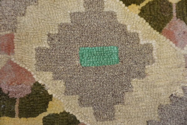 Nubby looped rug detail showing a geometric pattern in brown, cream, rust, and bright green.