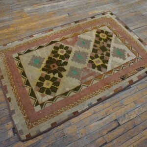 Small geometric rug in olive, dusty rose, and beige patterns laid on rustic wood planks.