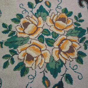 Highly textured rug detail showing gold and cream roses, green leaves, and a dark brown scalloped border.