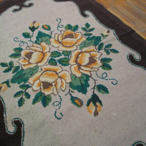 A high-pile floral rug with yellow roses, green leaves, and a dark brown scalloped border on a wood floor.