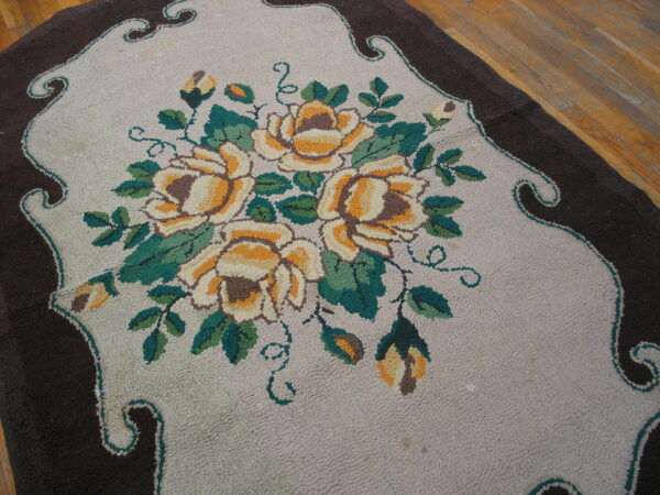 A high-pile floral rug with yellow roses, green leaves, and a dark brown scalloped border on a wood floor.