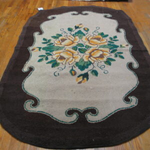Shaped hooked rug in dark brown and tan with yellow floral design on light wood floorboards.