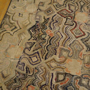 Abstract textured rug with variegated beige, gray, red, and navy accents rests on hardwood flooring.