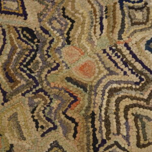 Textured hooked rug featuring an abstract geometric pattern in beige, brown, indigo, and soft accent colors.