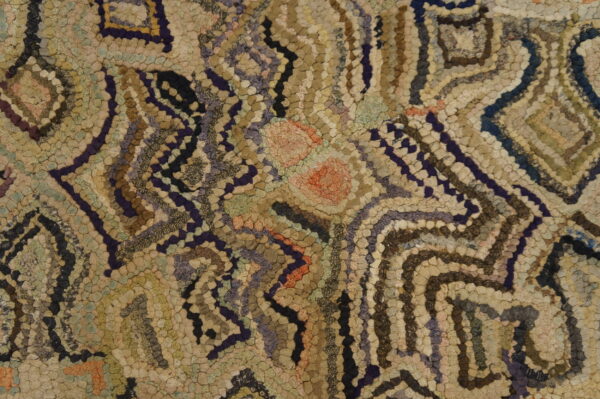 Textured hooked rug featuring an abstract geometric pattern in beige, brown, indigo, and soft accent colors.