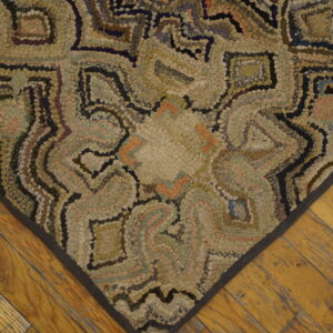 Muted, hooked rug with concentric earth-toned patterns is displayed on a rustic wood plank floor.