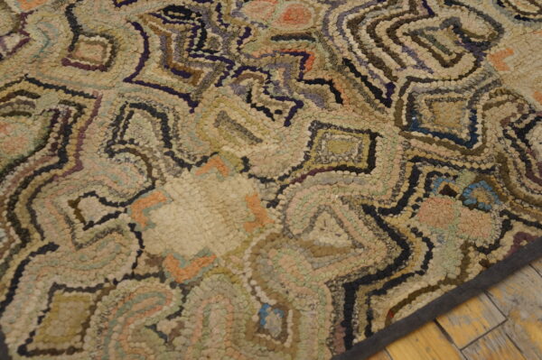 Muted hooked rug features abstract shapes in beige, green, orange, and dark brown on distressed wood flooring.