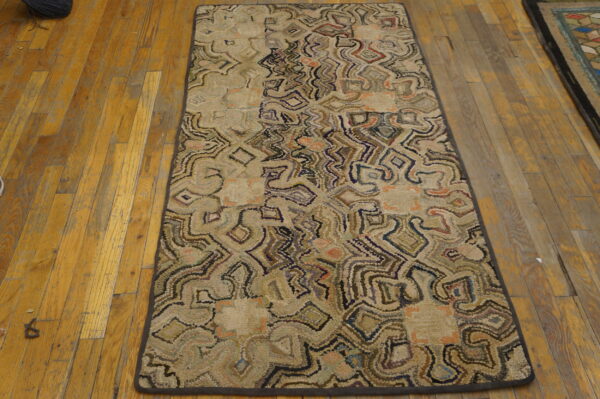Beige hooked runner rug with winding abstract patterns in brown, purple, and peach colors on a worn wood floor.