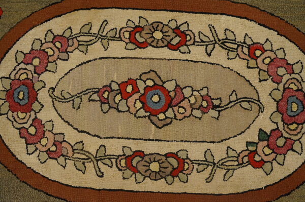 Oval hooked rug featuring a center taupe medallion surrounded by red, pink, and blue floral motifs.