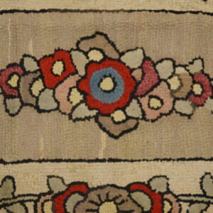 Detailed view of a textured rug showing red, blue, and pink flowers within a taupe framed pattern.