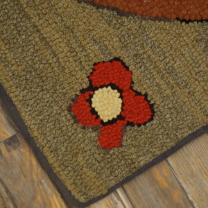 Textured olive green hooked rug with a red and cream floral pattern rests on weathered wood floors.