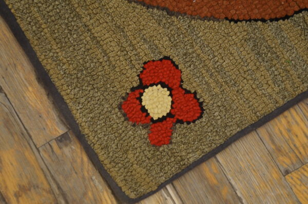 Textured olive green hooked rug with a red and cream floral pattern rests on weathered wood floors.