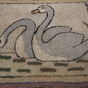 Close-up of a looped rug showing two gray swans among brown cattails and green water patches on a beige background.