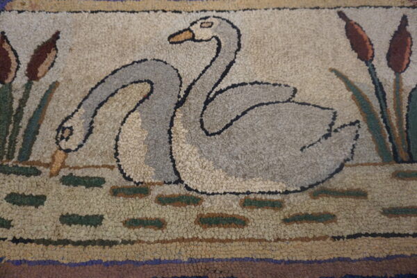 Close-up of a looped rug showing two gray swans among brown cattails and green water patches on a beige background.