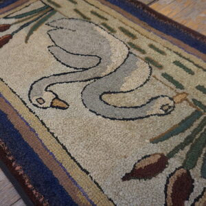 A hooked rug with a swan and cattail design in beige, gray, blue, and brown, lying on wood floors.