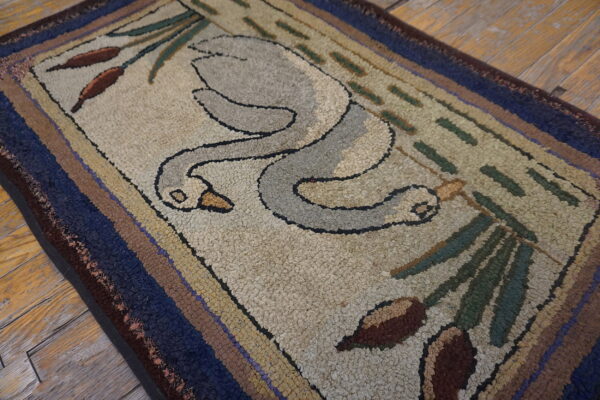 A hooked rug with a swan and cattail design in beige, gray, blue, and brown, lying on wood floors.