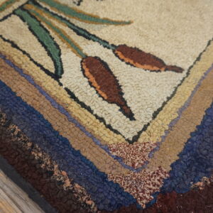 Chunky hooked rug detail showing brown cattails, green stems, and multicolored striped edges on wood planks.