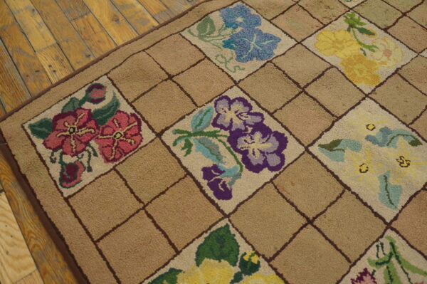 Beige hooked rug features a checkerboard lattice with colorful floral motifs on rustic wood planks.