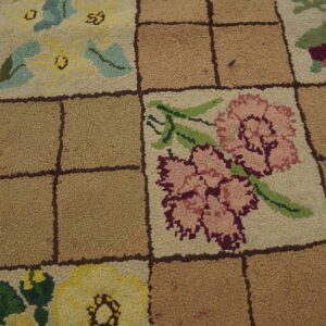 Close-up of a hooked rug featuring multicolored floral squares separated by solid tan squares in a grid pattern.
