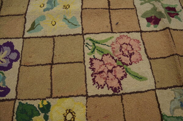 Close-up of a hooked rug featuring multicolored floral squares separated by solid tan squares in a grid pattern.