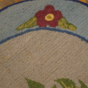 Round, looped pile rug detail shows a red flower on light blue and taupe fields over wood floor.