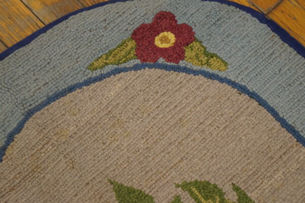 Round, looped pile rug detail shows a red flower on light blue and taupe fields over wood floor.
