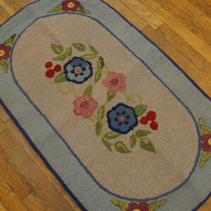 Oval rug with blue and pink floral design and light blue border rests on distressed wooden floorboards.
