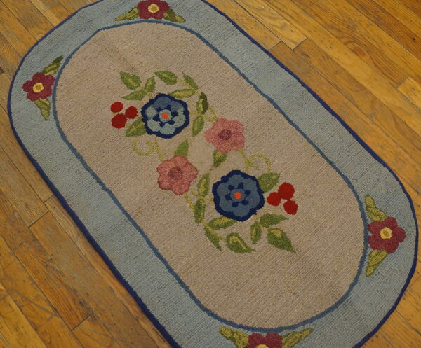 Oval rug with blue and pink floral design and light blue border rests on distressed wooden floorboards.