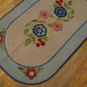 Oval beige rug with pink and blue floral design and a dusty blue border, set on wood plank flooring.