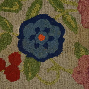 Close-up of a hooked texture rug featuring a floral pattern with blue, red, pink, and green on a gray background.