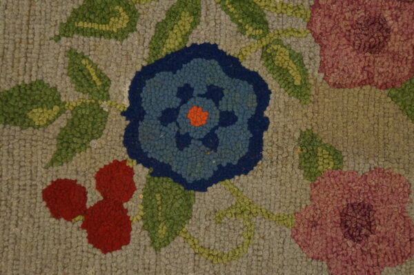 Close-up of a hooked texture rug featuring a floral pattern with blue, red, pink, and green on a gray background.