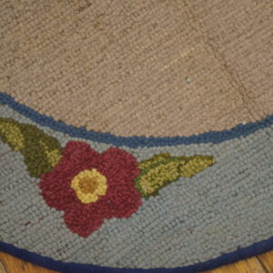 Close view of a looped beige and light blue rug with a central red and yellow floral design on a wood floor.