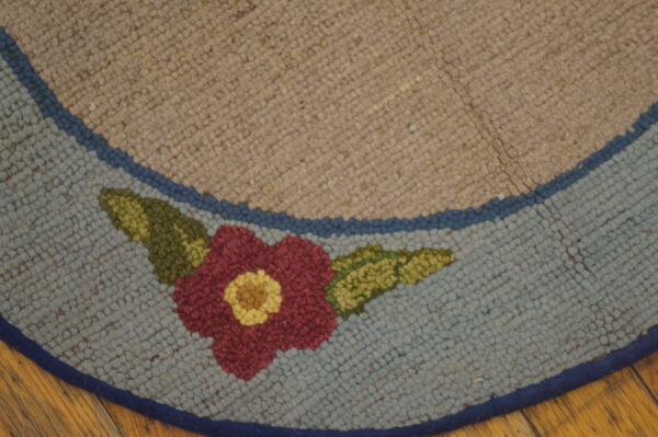 Close view of a looped beige and light blue rug with a central red and yellow floral design on a wood floor.