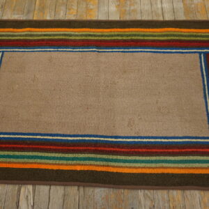A textured tan rug featuring a multicolored striped border rests on distressed gray and yellow wood.