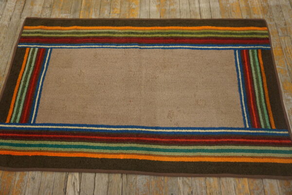 A textured tan rug featuring a multicolored striped border rests on distressed gray and yellow wood.