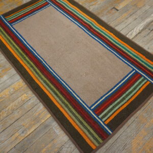 A low-pile taupe rug with a wide, bright striped border rests on distressed gray wood planks.