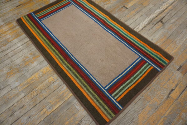 A low-pile taupe rug with a wide, bright striped border rests on distressed gray wood planks.