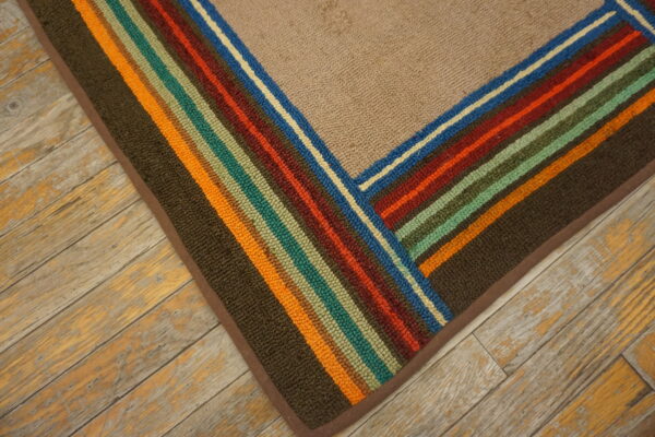 Beige textured rug corner featuring borders of multicolor stripes on distressed wood planks.