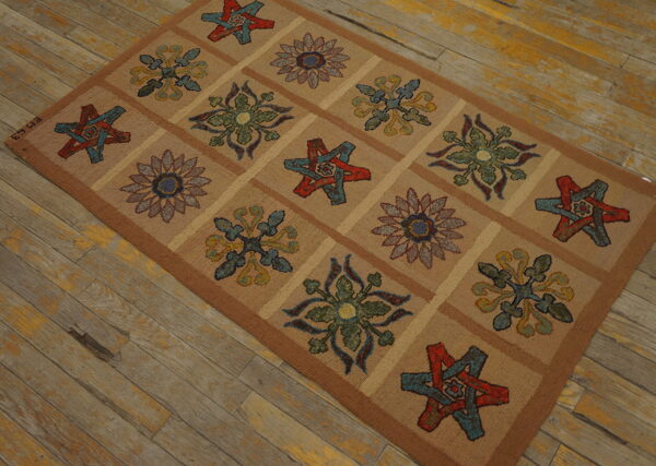 Low-pile tan rug with a colorful grid of floral and star motifs bordered in brown, resting on distressed wood planks.