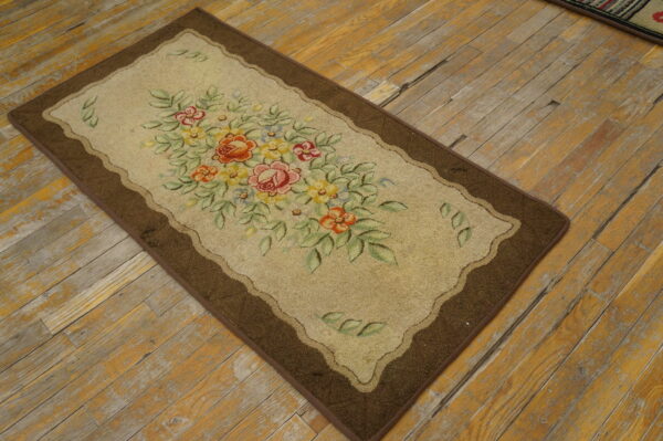 Low-pile beige accent rug with a bright floral bouquet and a dark brown border on weathered wood flooring.