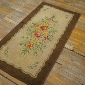 A floral runner rug with a brown border and tan field sits angled on weathered wooden plank flooring.