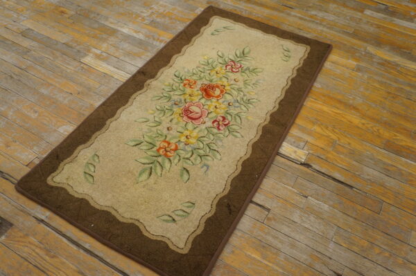 A floral runner rug with a brown border and tan field sits angled on weathered wooden plank flooring.