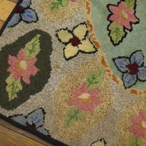 Muted floral hooked rug with pink, blue, and green flowers rests on distressed wooden planks.