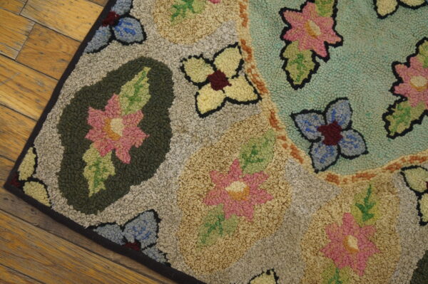 Muted floral hooked rug with pink, blue, and green flowers rests on distressed wooden planks.