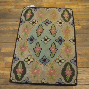 Textured floral hooked rug featuring a blue medallion and pink flowers on worn wooden planks.