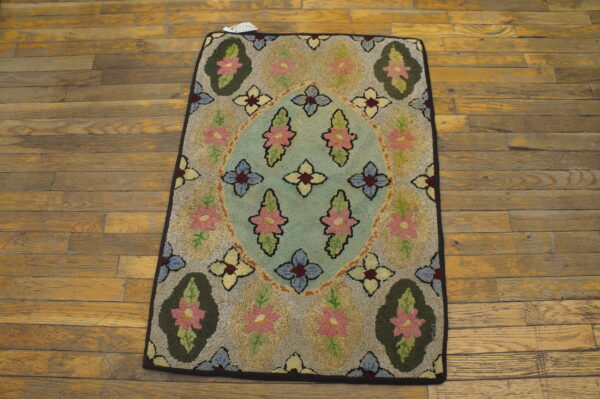 Textured floral hooked rug featuring a blue medallion and pink flowers on worn wooden planks.